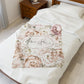 Floral patterned blanket with personalized text on a bed in a bedroom setting.