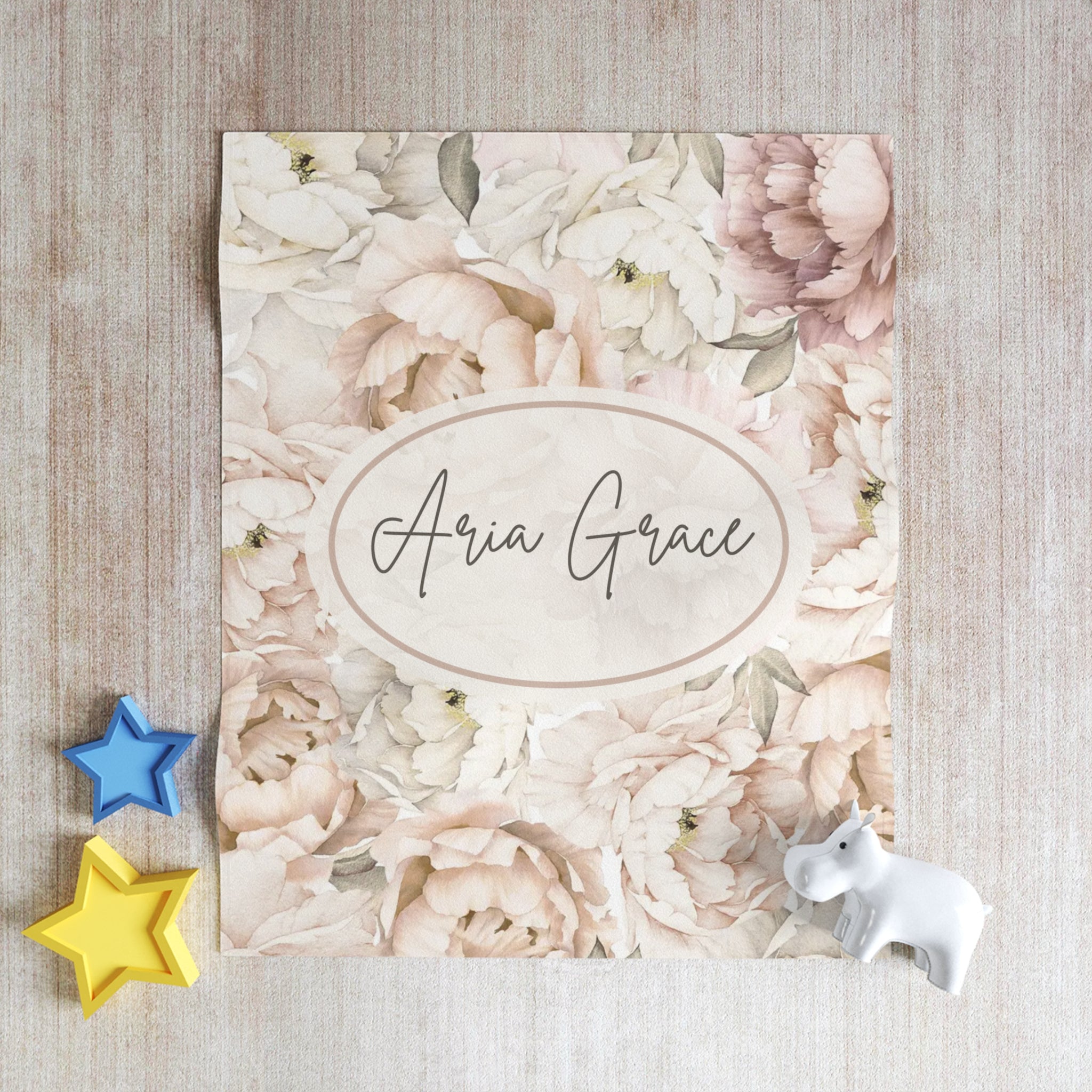 Floral blanket design with personalized text on a textured surface with star and unicorn toys.