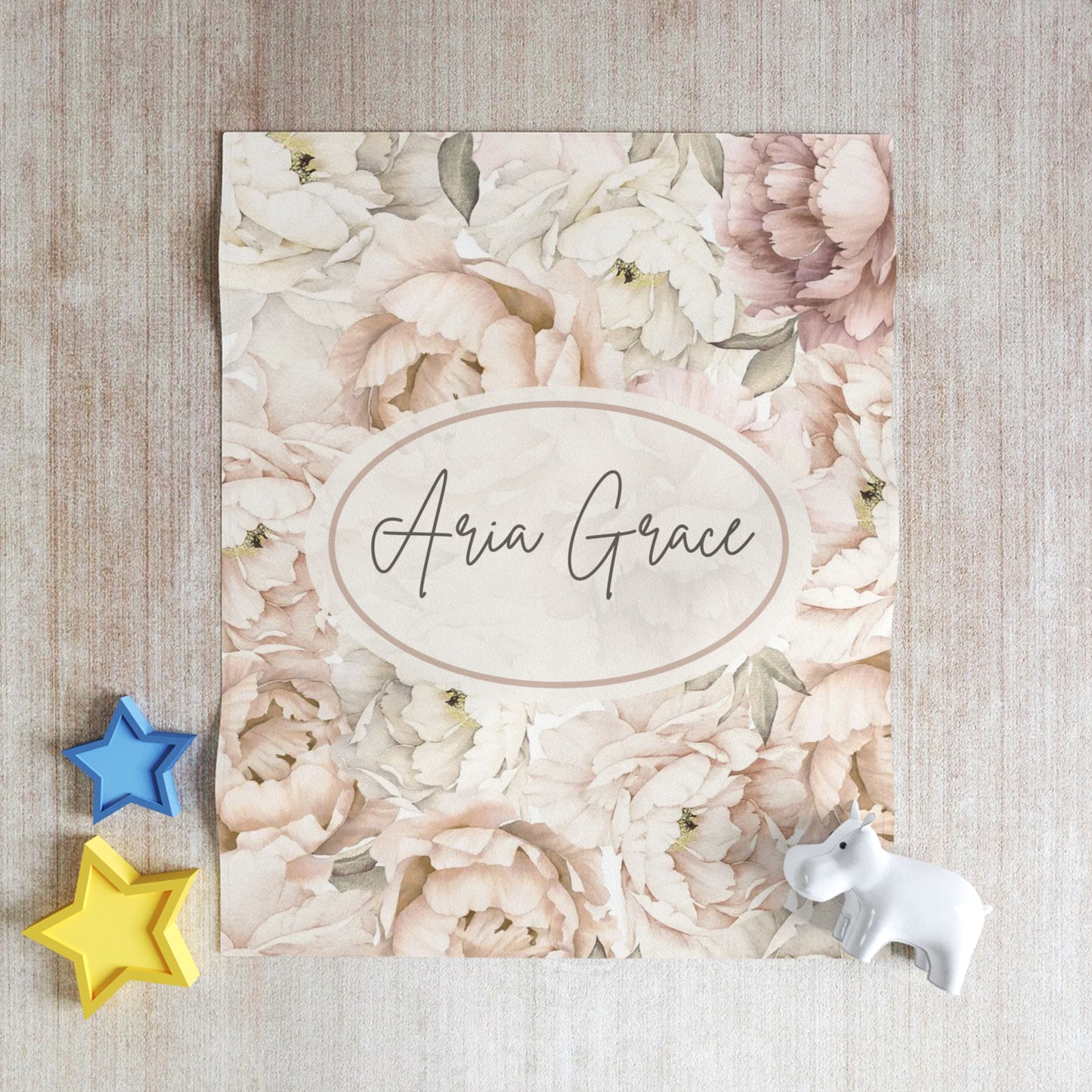 Floral blanket design with personalized text on a textured surface with star and unicorn toys.