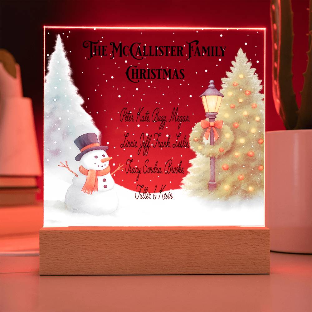 Decorative Christmas sign with a snowman, tree, and family names on a red background.